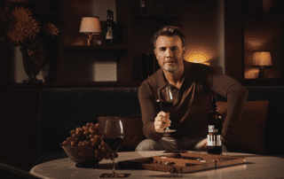 Gary Barlow standing beside a table with wine bottles.